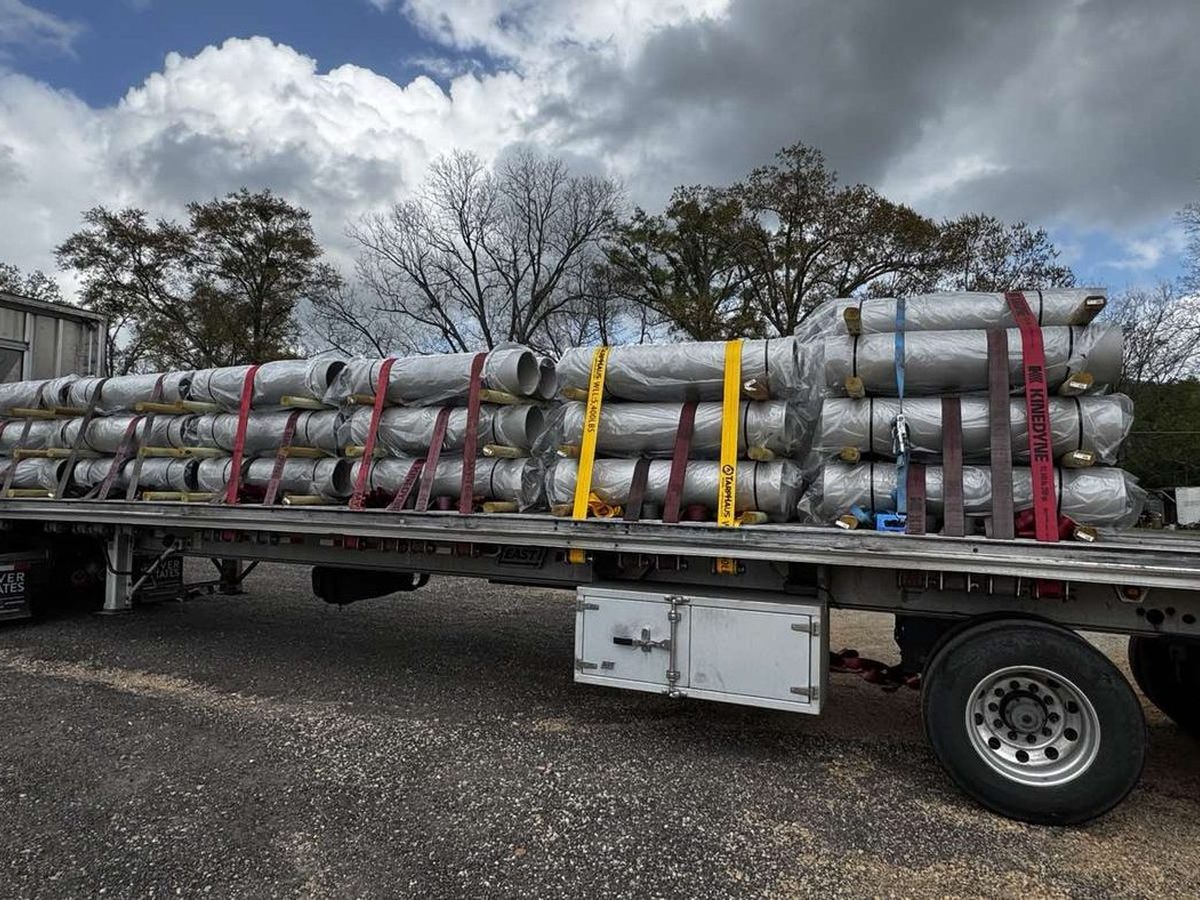 Flatbed truck loaded with wrapped stainless steel bollards bound for Detroit Metropolitan Airport