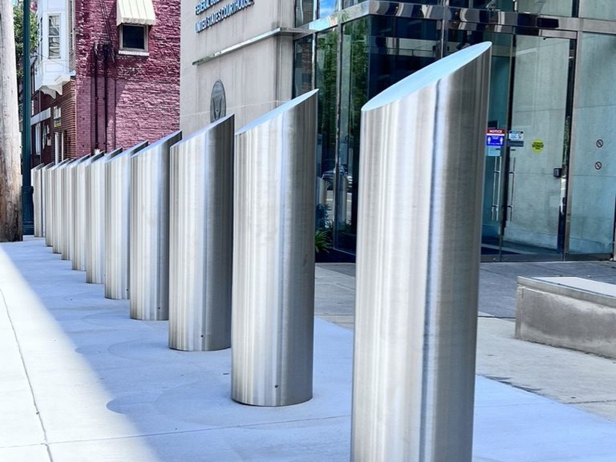 Row of brushed stainless steel slope-top M50 crash-rated bollards outside a federal courthouse