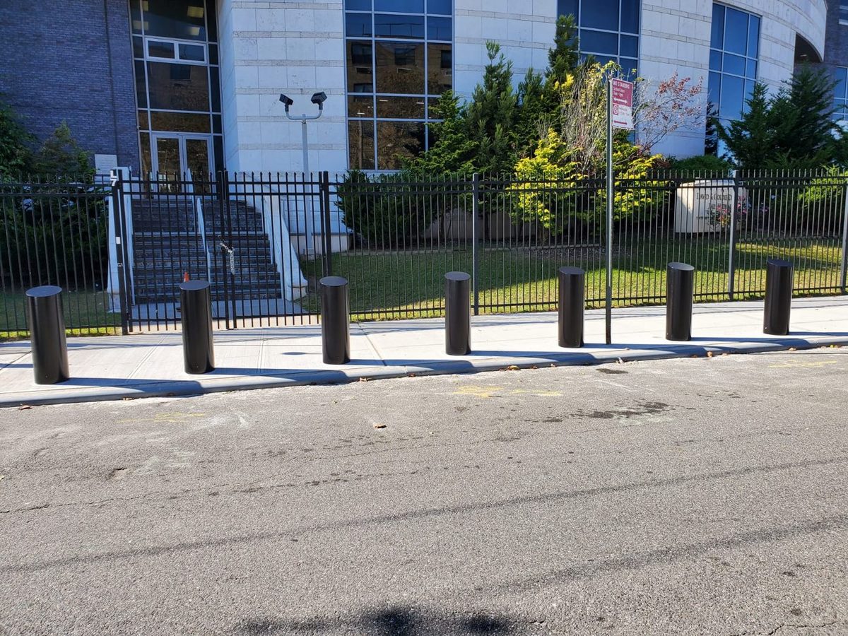 Row of black flat-top fixed security bollards along a perimeter fence at a New York City facility