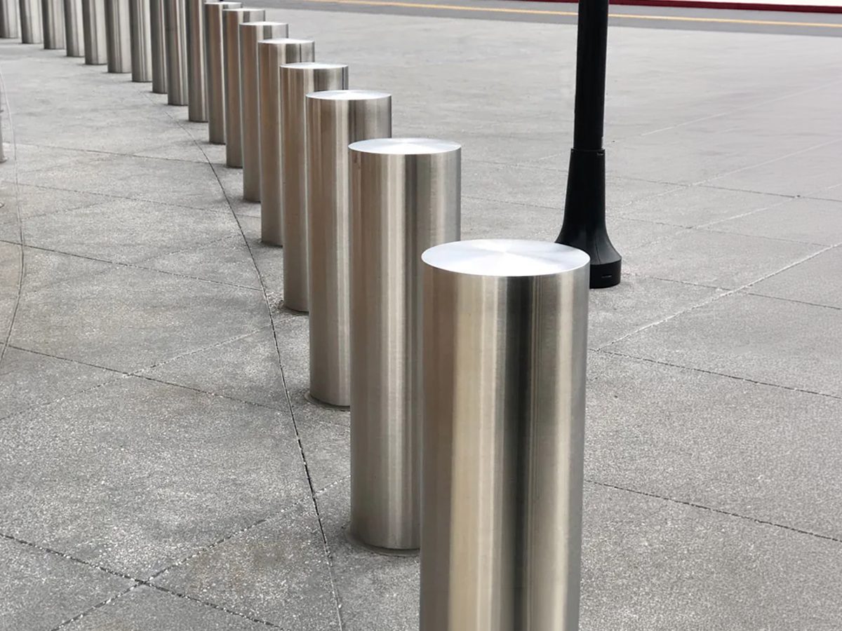 Row of brushed stainless steel embedded security bollards curving along a city sidewalk